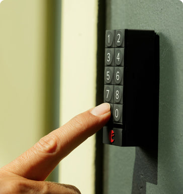 A persons finger pushes a button on a black August Home keypad door lock